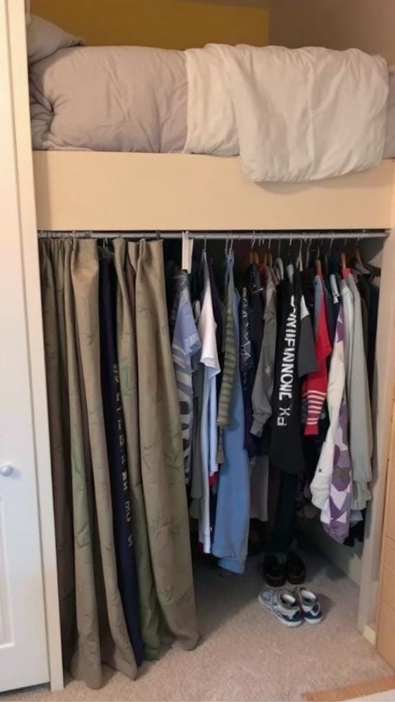 A bunk bed with a curtain closet underneath, featuring clothes hanging and a bed below.