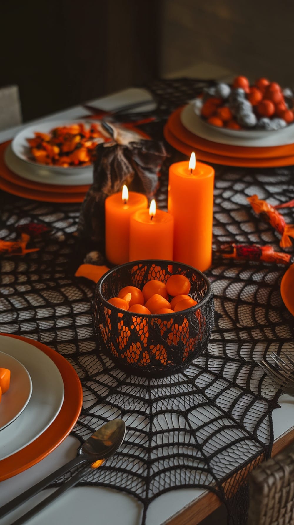 A table set with a spider web tablecloth, orange candles, and Halloween-themed snacks.