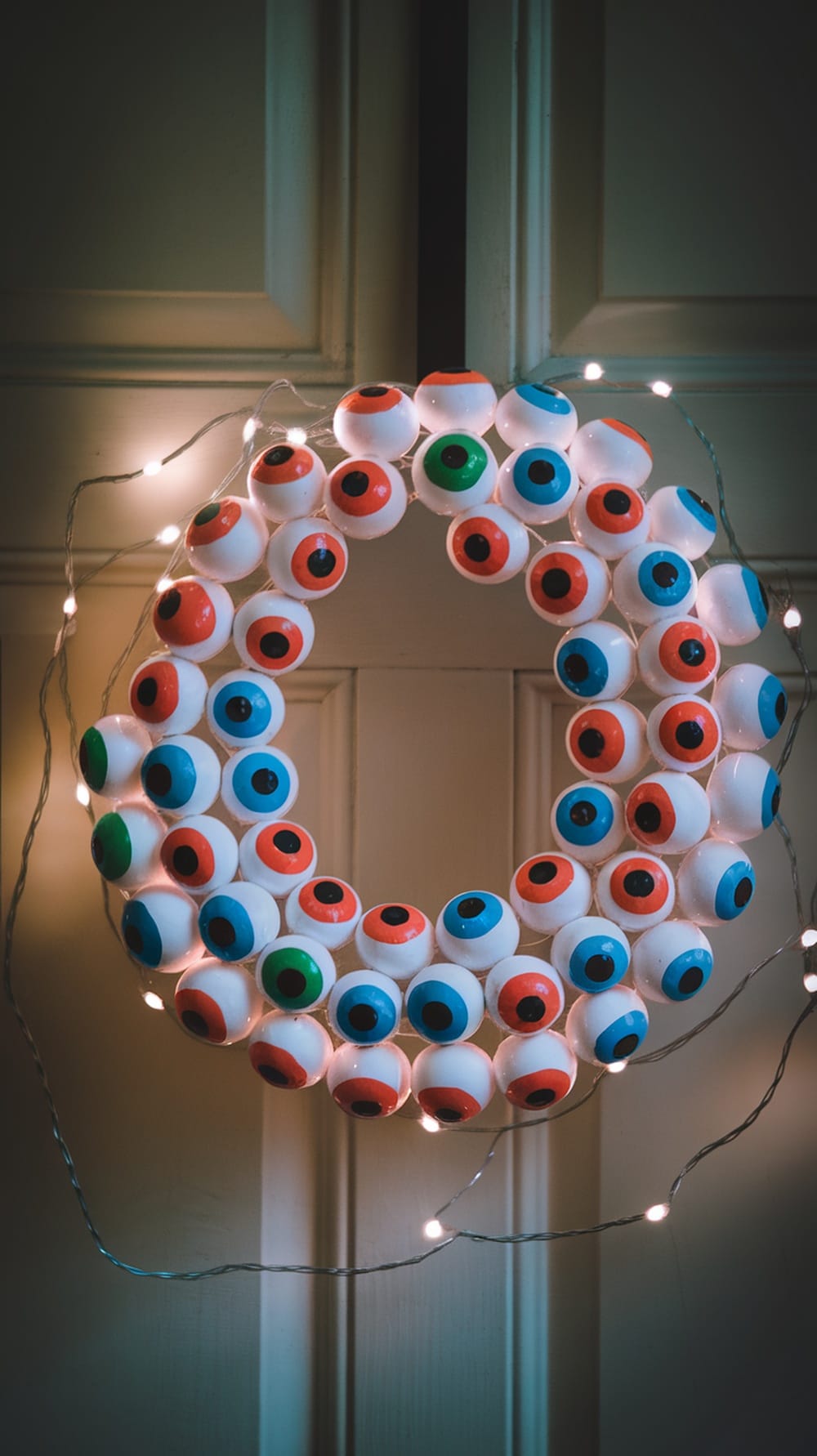 A wreath made of colorful eyeballs with fairy lights, hanging on a door.