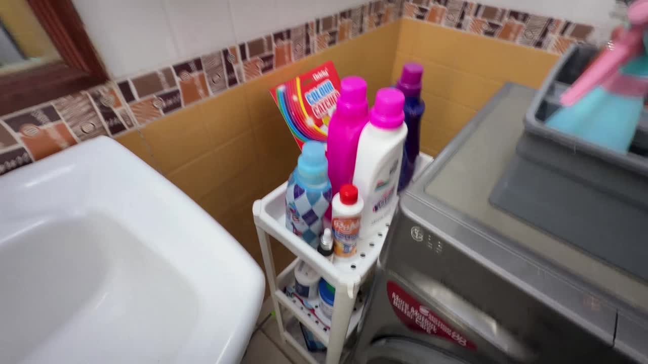 Three-tier laundry supply rack beside the washing machine with detergent bottles within reach