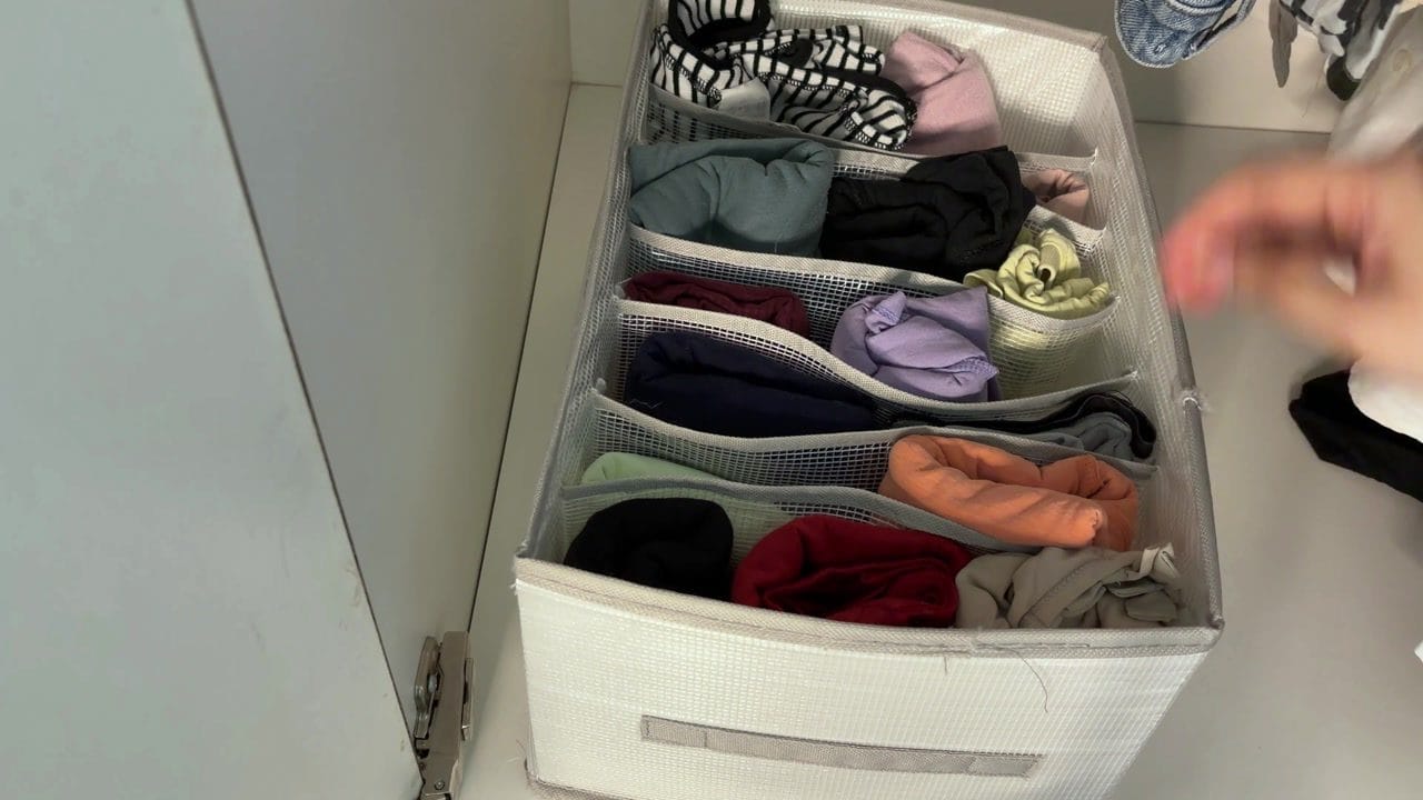 Rolled clothes stored upright in separate compartments of a file-style closet organizer.